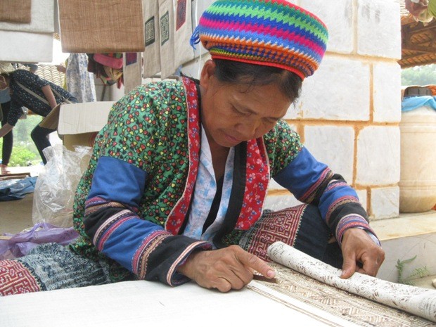 Giới thiệu tới du khách cách vẽ hoa văn thổ cẩm lên tấm vải bằng thanh tre quết mật ong rừng đun nóng, nét văn hóa của dân tộc Mông (tỉnh Hà Giang)
