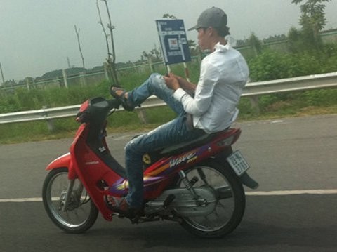 Nam thanh niên vừa điều khiển xe máy bằng chân vừa nhắn tin điện thoại. Ảnh. Vnmedia.