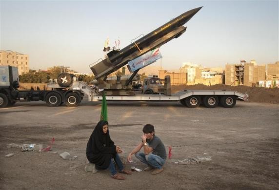 Hai người đang ngồi nghỉ cạnh tên lửa Zelzal do Iran sản xuất trong một triển lãm quân sự.