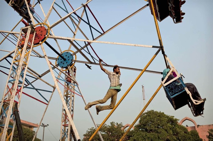 Một người đàn ông treo mình trên một bánh xe đu quay tại một hội chợ ở New Delhi, thành phố thường xuyên bị mất điện và người ta buộc phải dùng tới cách thủ công này để vận hành các khu vui chơi hôm 19/11.