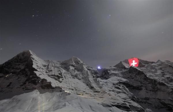 Lá quốc kỳ Thụy Sỹ bằng ánh sáng khổng lồ chiếu sáng mặt phía bắc của ngọn núi Jungfrau (trái) và Moench (giữa) tại Bernese Oberland ngày 1/1 dân dịp kỷ niệm 100 năm ngày đưa tuyến đường sắt Jungfrau đi vào hoạt động. Lá quốc kỳ khổng lồ trên được đặt tại nhà ga cao nhất của châu Âu, ga Jungfraujoch, ở độ cao 3.454 m.