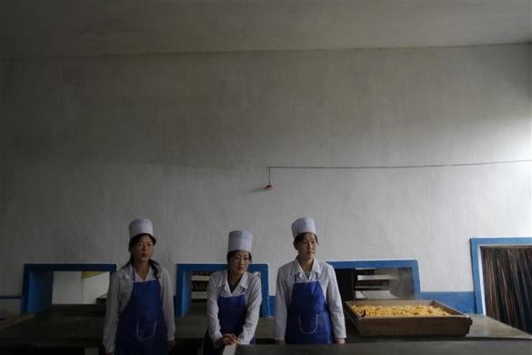 Những người phụ nữ đứng bên cạnh khay đựng thức ăn chế biến từ ngô dành cho trẻ mồ côi tại khu vực bị thiệt hại bởi bão lũ gần tỉnh Bắc Hwanghae ngày 29/9/2011.
